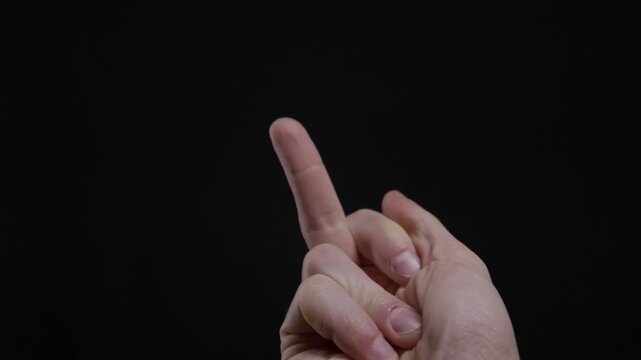 A man's hand makes a scolding gesture, wagging an index finger to say no against a solid black background. Concept of disapproval, warning, denial, and forbidding an action.