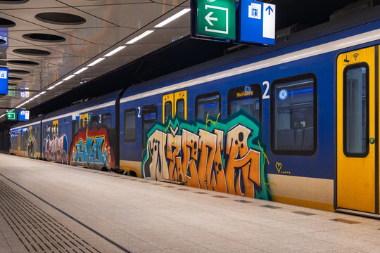 A Dutch passenger train at Schiphol station covered in vibrant street art graffiti, highlighting urban culture and public transport in Holland