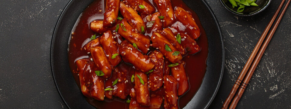 Traditional Korean tteokbokki served on black plate with chopsticks and sesame seeds on black rustic