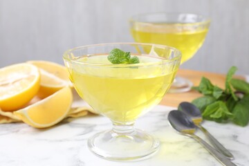 Fototapeta premium Yummy yellow jelly in dessert bowls, mint and fresh lemons on white marble table, closeup
