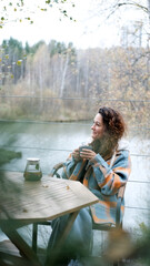 A sweet woman with curly hair drinks tea and relaxes on the terrace of her house on an autumn day. Health care, sincerity, a sense of balance and calm.