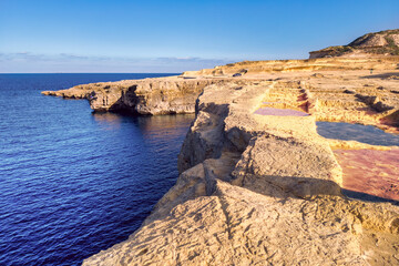 Salt pans on rocky coastline overlooking the blue Mediterranean Sea near Zebbug, Gozo, Malta