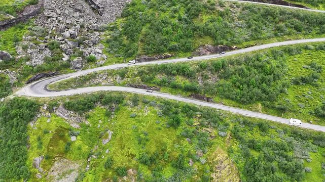 Forward drone flight, drone view of S road, S curve in the Italian dolomites, some cars and motercycles are driving on the road, taking curves. Steep mountain pass  surrounded by greenery, grass and t