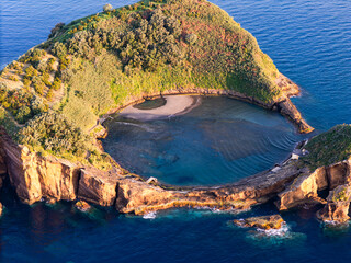 Natural ocean lagoon inside volcanic islet with boats anchored nearby, sunny coastal scene of Azores, drone view