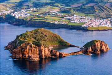 Coastal volcanic islet with bright lagoon water contrasting with dark outer ocean on Sao Miguel island, Azores, drone footage