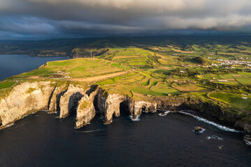 Rugged Atlantic shoreline with dark volcanic cliffs and narrow sea channels in warm evening tones. Aerial drone Azores
