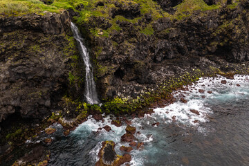 Coastal waterfall surrounded by black volcanic rocks and green vegetation, Sao Miguel Island, Azores