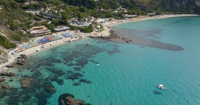 Aerial view Grotticelle beach, in Calabria, Southern Italy. Panorama of the Calabrian coast featuring a beautiful beach, lush green hills, vibrant turquoise waters, and submerged rocky reefs.