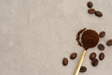 Ground coffee in spoon with coffee beans on beige background, top view