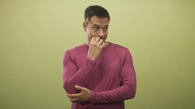 Young hispanic man with moustache wearing magenta long sleeve shirt biting nails with fingers to mouth in studio; anxiety doubt contemplation.