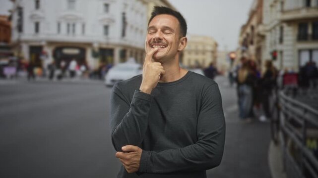 Hispanic man with moustache touching chin with finger, smiling in a busy street with buildings and pedestrians; playful curiosity.
