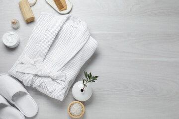 Flat lay composition with bathrobe and spa essentials on white wooden background. Space for text