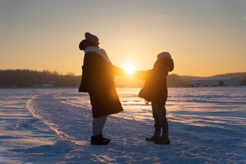 Mother and Daughter Holding Sun in Hands Together on Snowy Lake at Golden Hour, Magical Winter Sunset