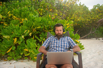 Remote Worker Using Laptop on Tropical Beach with Headphones