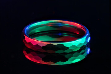 A color‑lit faceted tungsten ring on a black glossy surface.