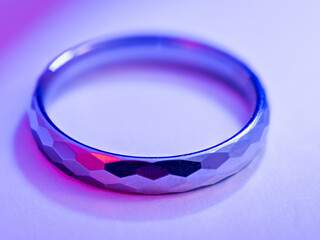 A pink‑purple lit faceted tungsten ring on a white background.