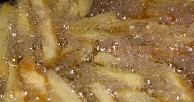 overcooked orange French fries in hot sunflower oil during frying in a pan, delicious fast food yellow thawed and fried French fries in hot oil
