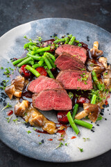 Roasted venison tagliata steak from haunch with wild Mushrooms volvaria volvacea, green beans vegetable and fruity sauce with red wine and wild herbs served as close-up on a design plate