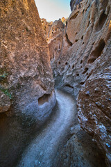 Obraz premium Narrow Slot Canyon Trail with Rugged Rock Walls and Natural Holes in Desert Landscape