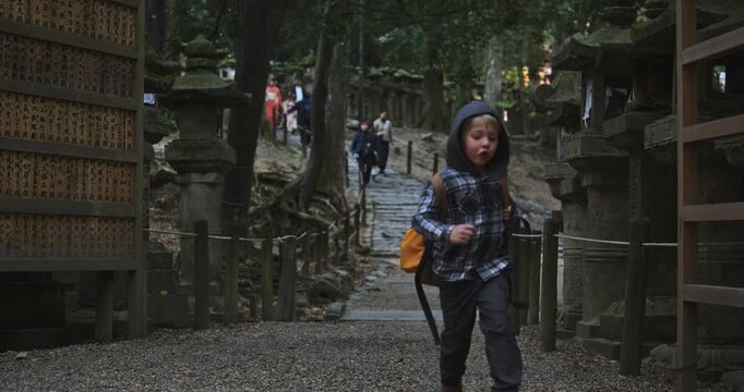 Little boy with backpack running towards camera in ancient Japanese shrine area