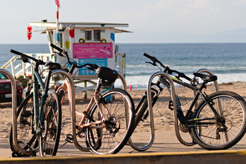Obraz premium Bicycles secured to rack on sandy California beach with lifeguard tower and ocean waves in background.