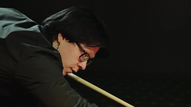 Portrait of young caucasian man with black hair, glasses and calm expression lining up shot in billiard club, focused technique and steady grip of cue, social pastime and weekend session among friends