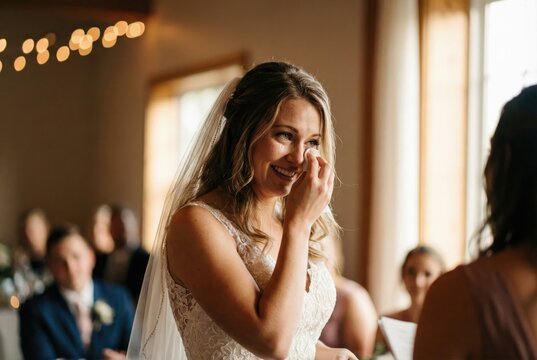 A bride emotionally wipes away a tear of joy while smiling during her wedding ceremony.