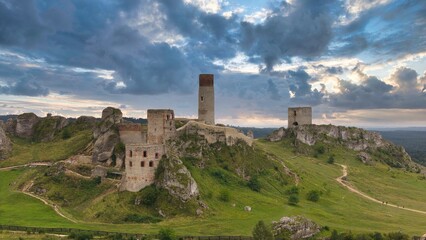 Castle ruins in Olsztyn near Częstochowa captured in golden hour light, aerial drone view over limestone rocks and historic fortress in Poland