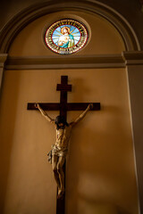 Large Wooden Crucifix with Stained Glass Window in Church, Catholic Sanctuary Interior with Jesus on the Cross and Sacred Heart Art, Solemn Christian Symbols of Faith and Sacrifice 