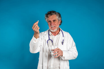 Senior doctor in lab coat with stethoscope holding a white pill and offering medication with a confident expression
