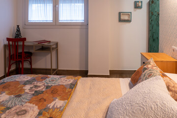 Bedroom featuring a floral bedspread, red wooden chair, and desk by the window, creating a cozy and stylish home interior