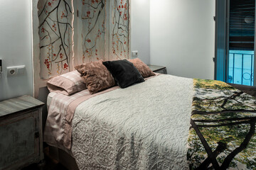 Bedroom interior showcasing a comfortable bed with patterned quilt, decorative headboard, nightstand, and window view