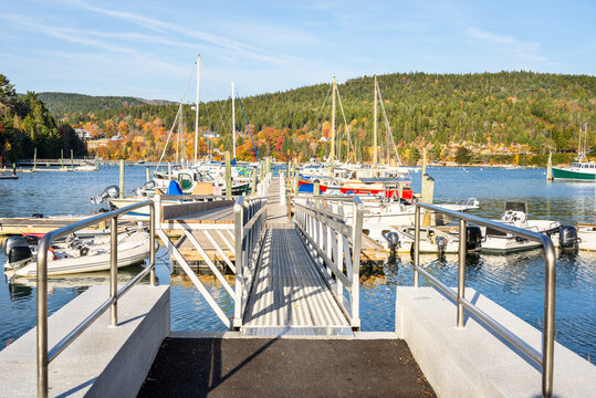 Motorboats and siling boats moored to a wooden floating jetty in a harbour on a sunny autumn day