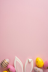 Obraz premium Soft vertical pink backdrop sets a gentle mood for Easter greetings. Colorful eggs and bunny ears create a playful, festive scene perfect for seasonal cards and promotions