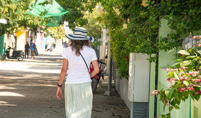 Woman walking on tropical street with flowers and scooters in island town