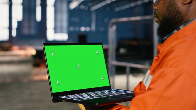 Green screen next to operator using laptop and industrial equipment to support construction and production tasks on the factory floor. Heavy machinery, tools and organized workflow.