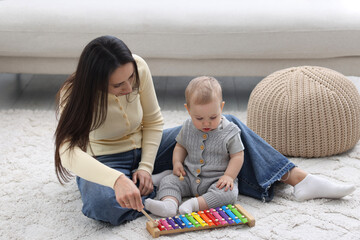 Naklejka premium Mother and her baby boy playing with toy xylophone at home