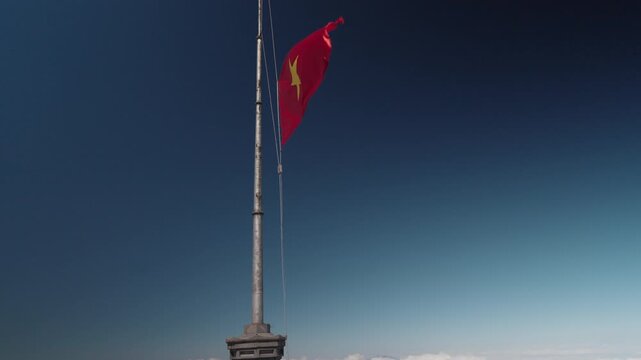 Vietnamese national flags waving at Fansipan Peak in Sapa, Vietnam, with visitors at the summit under a clear blue sky, symbolizing national pride, travel, and achievement at Vietnam&rsquo;s highest mountai