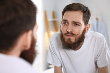 Fototapeta premium Handsome man looking at his beard and mustache in mirror at home