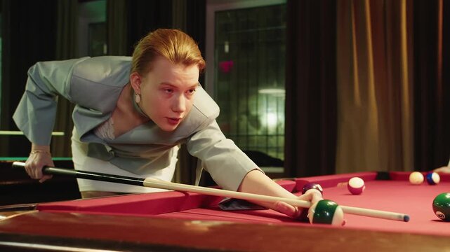 Single player lady concentrates on aiming shot. Young adult caucasian blonde woman in blazer executes precise shot in club vintage environment. precise hit of white cue ball on red table for billiards