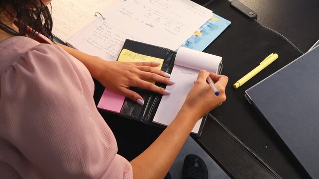 Close-up of a woman writing in her planner at a desk. The image conveys organization, planning, productivity, and focus on tasks in a modern work or study environment.