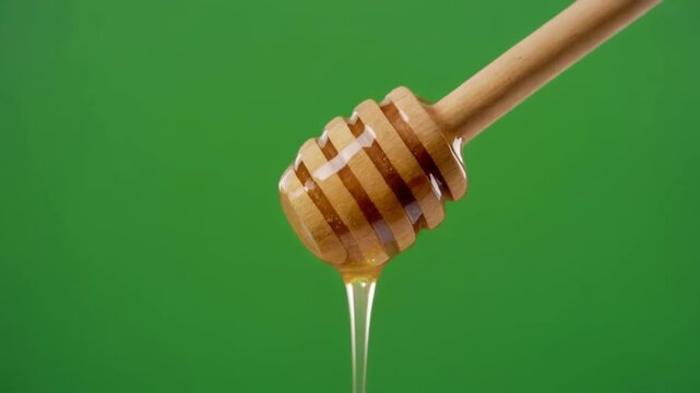 Closeup of a wooden honey dipper dripping golden honey against a vibrant green screen background.