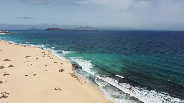 Aerial drone flight over Corralejo dunes towards turquoise Atlantic waters with Isla de Lobos in the distance