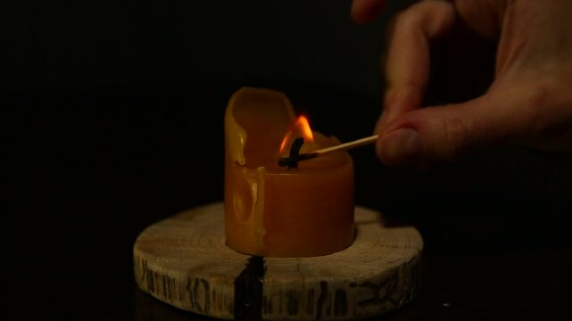Woman hand lights a match the bees wax candle on wooden candlestick for mood, relaxation, meditation dark red background. Person lighting the decoration single candle flame