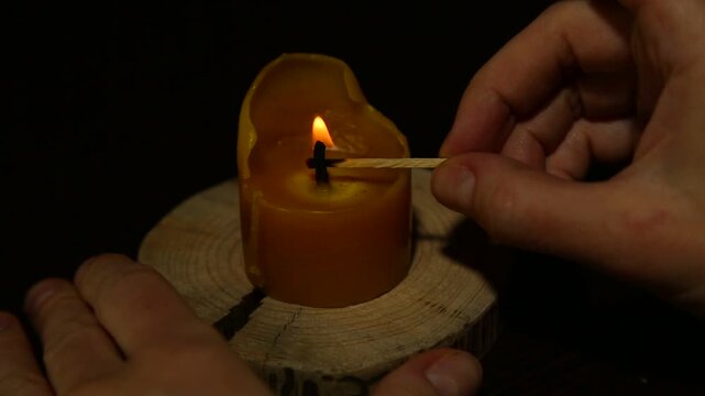 Woman hand lights a match the bees wax candle on wooden candlestick for mood, relaxation, meditation dark red background. Person lighting the decoration single candle flame