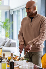Indian friends gathering at open-plan dining area, man carving roast poultry and pouring juice © wavebreak3