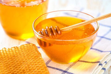 Glass bowl with sweet honey and honeycombs on white table.