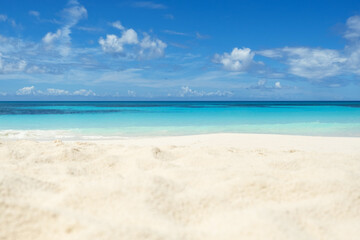 White soft sand against the backdrop of the ocean and blue sky with clouds. A tropical summer turquoise sea.