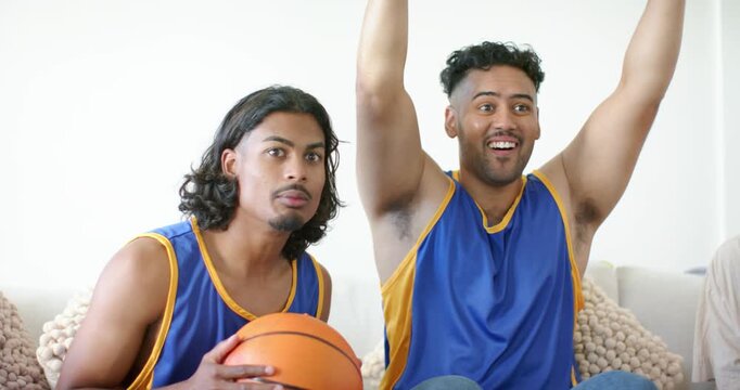 African American fans in blue-yellow kits reacting to score on TV, gripping basketball, cheering