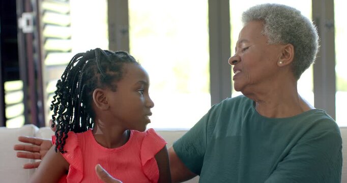 Senior woman and girl puckering, drawing granddaughter in and hugging for affection on couch